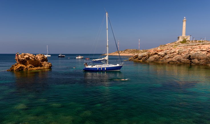 Velero navegando cerca del faro en el Cabo de Palos, Murcia